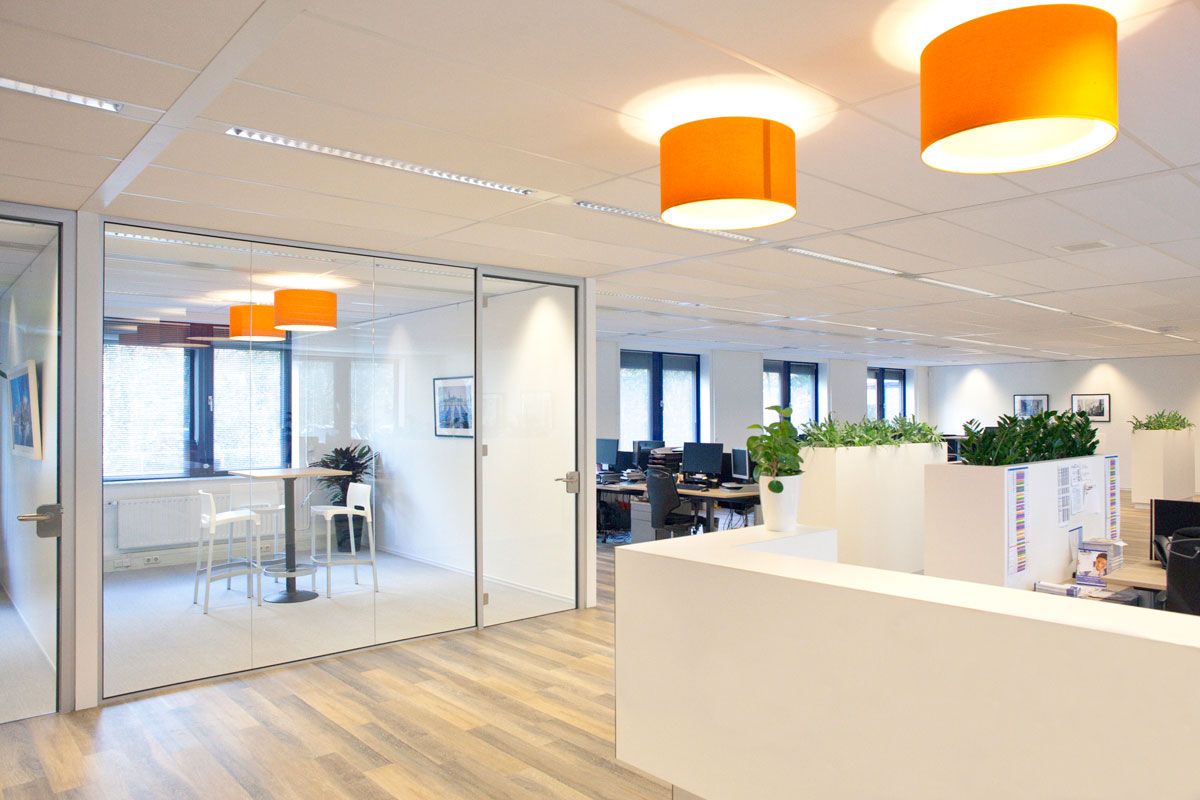 Inrichting kantoor in Zeist met glaswanden, houten vloeren en oranje hanglampen, voorzien van werkplekken en planten.